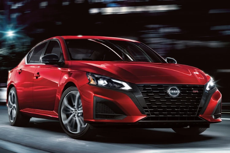 Red Nissan sedan driving through a city at night