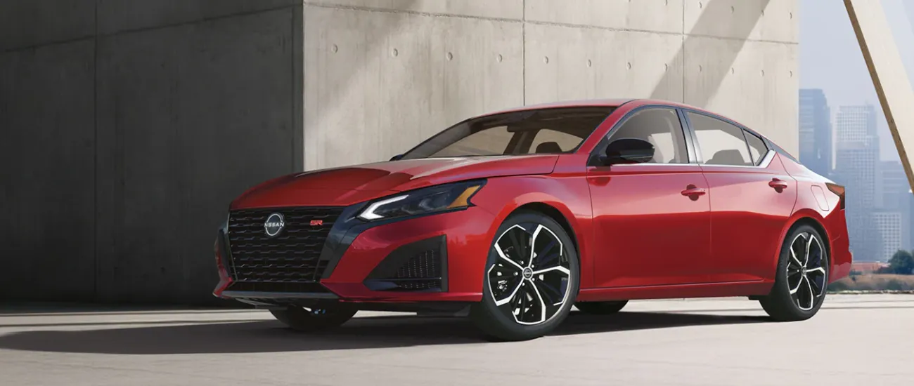 Red Nissan sedan parked beside a concrete building