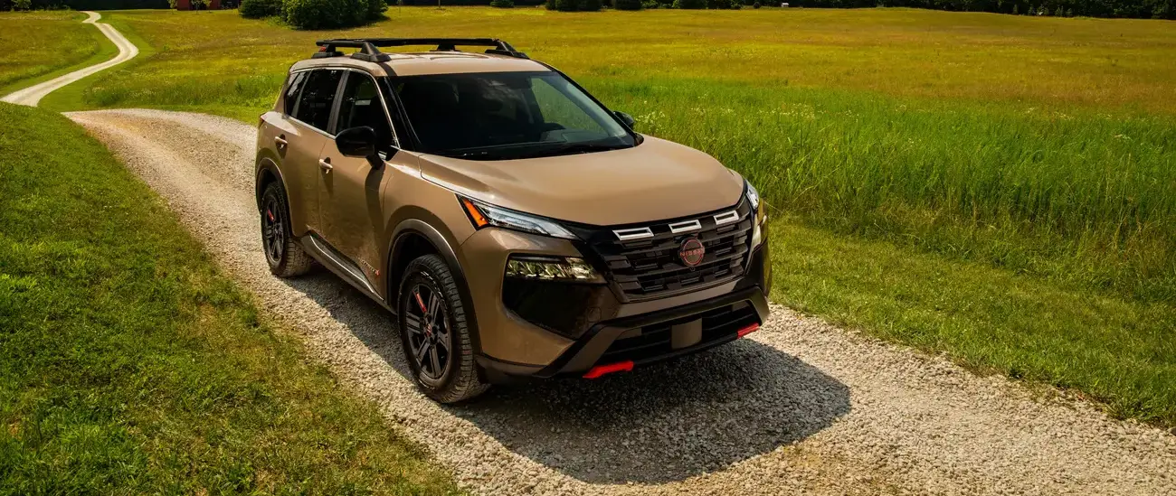 Nissan Rogue parked on a gravel path through a green field