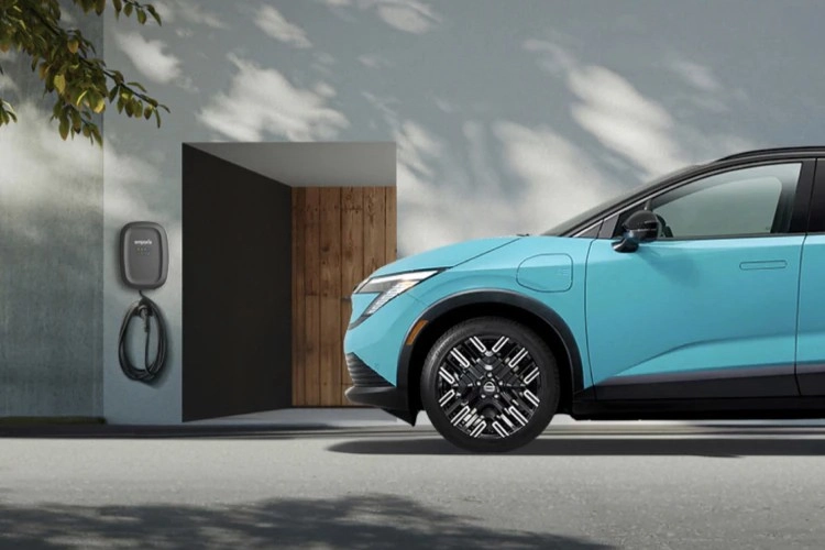 Teal Nissan LEAF charging from a wall-mounted home charger on a driveway