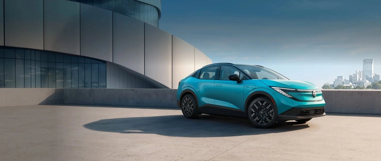 Teal Nissan LEAF parked in front of a curved concrete building