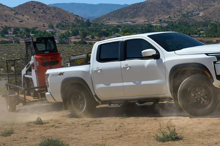 White Nissan Frontier towing a trailer on a mountain road