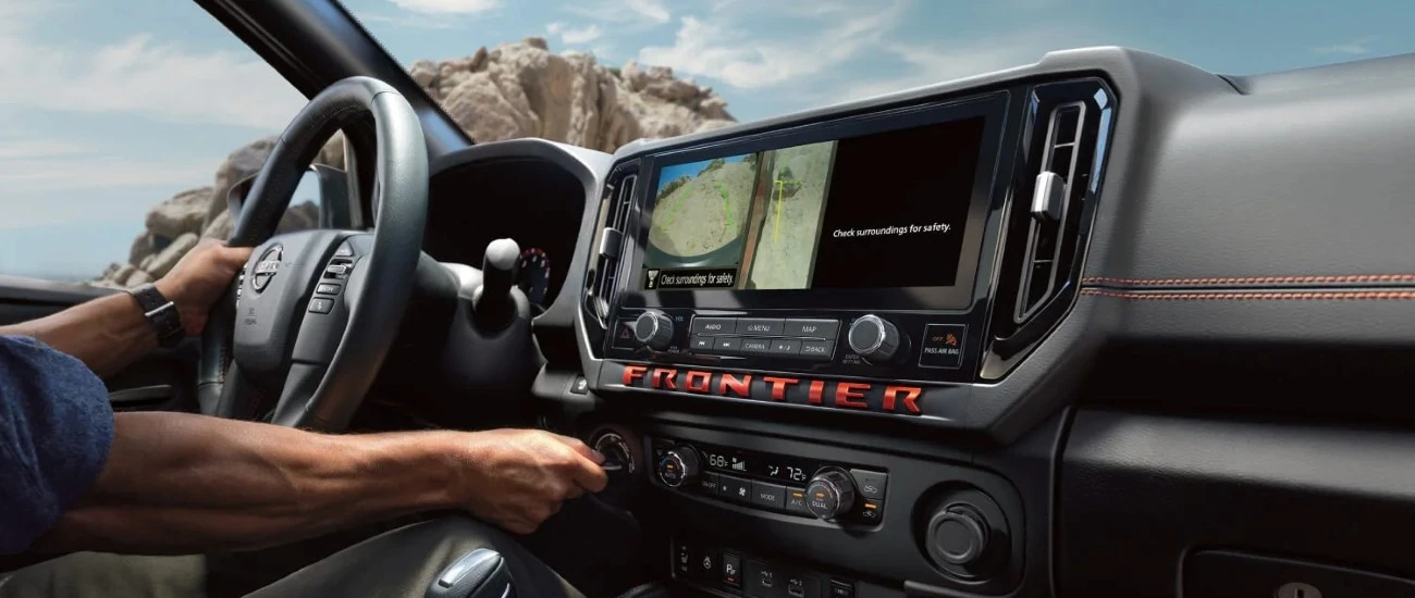 Driver's hands on the Nissan Frontier steering wheel with the centre touch-screen display lit up