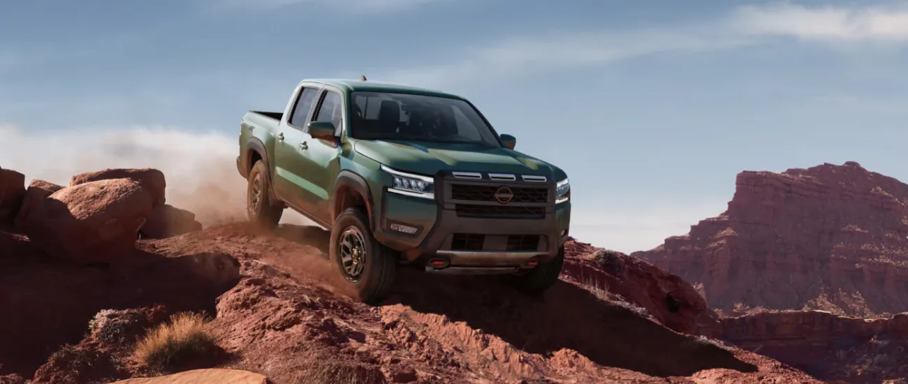 Green Nissan Frontier truck driving off-road through red rock terrain