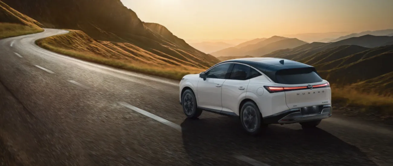 White Nissan SUV driving on a winding mountain road at sunset
