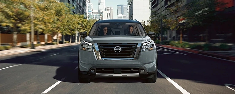 Front of a Silver 2025 Nissan Pathfinder® Driving in the City with a Man and a Woman Inside